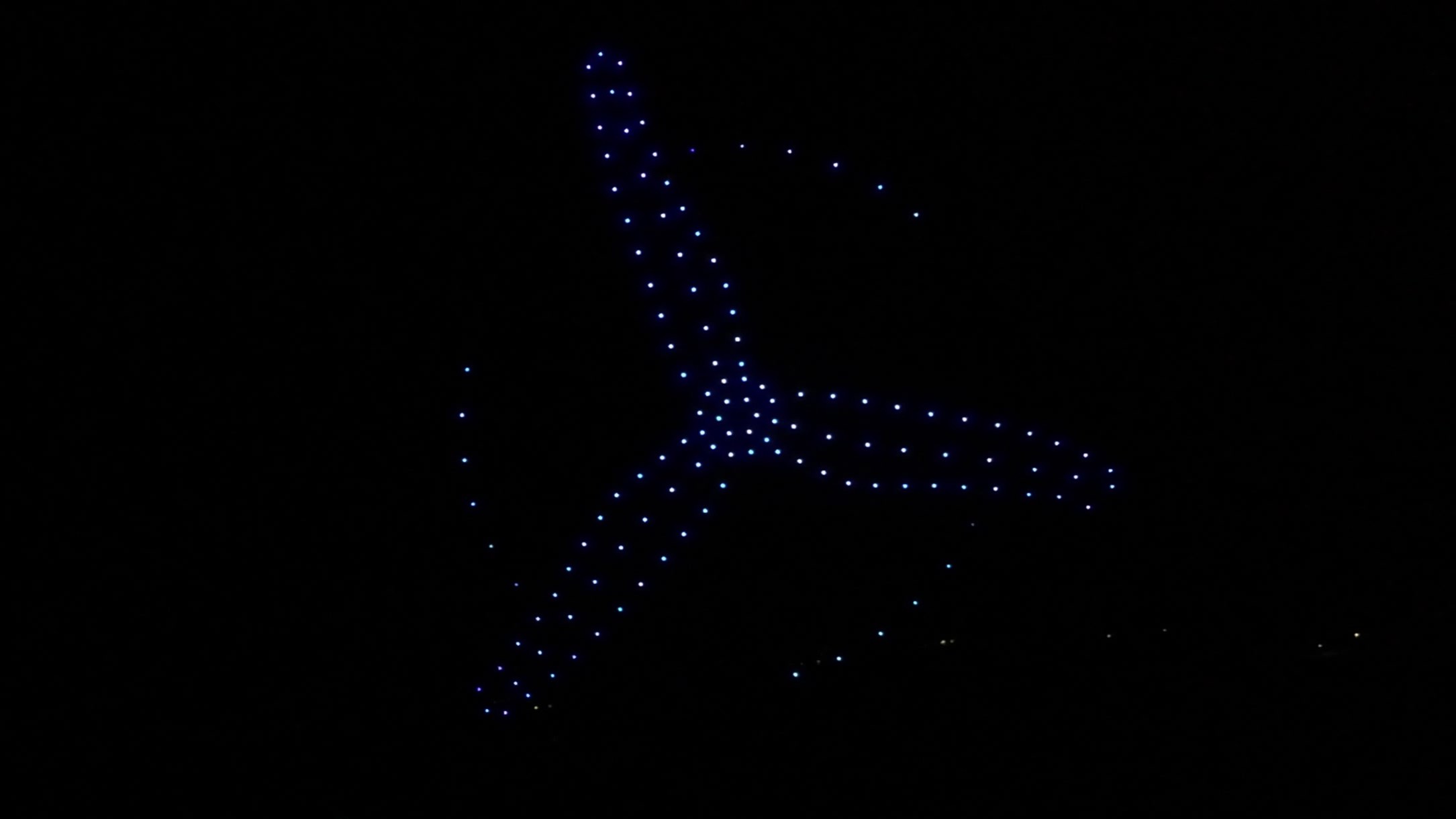 A drone light show formation lit in gold above a nighttime crowd